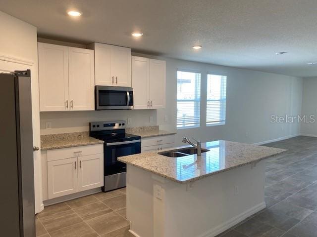 kitchen with light stone counters, a center island with sink, white cabinets, and stainless steel appliances