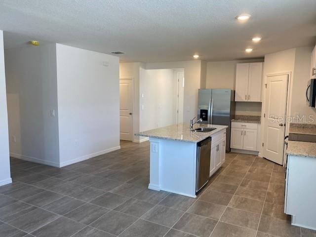 kitchen featuring light stone countertops, appliances with stainless steel finishes, white cabinetry, and a kitchen island with sink