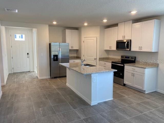 kitchen with light stone counters, stainless steel appliances, a kitchen island with sink, sink, and white cabinets