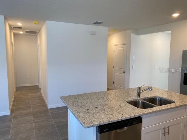 kitchen with dishwasher, white cabinets, a center island with sink, sink, and light stone counters