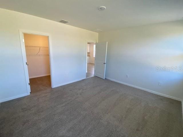 unfurnished bedroom with a spacious closet, a closet, and dark carpet