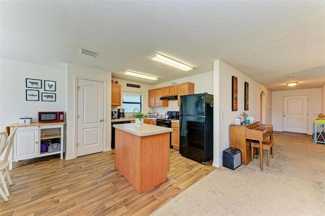 kitchen featuring a textured ceiling, light hardwood / wood-style floors, a kitchen island, and black appliances