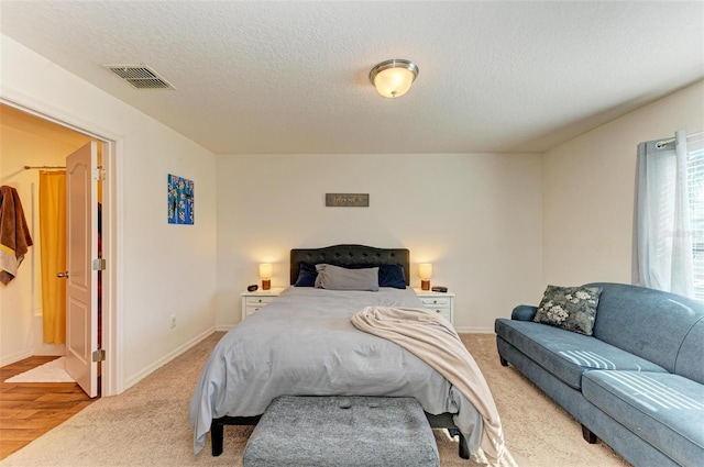 bedroom with light wood-type flooring, a textured ceiling, and connected bathroom