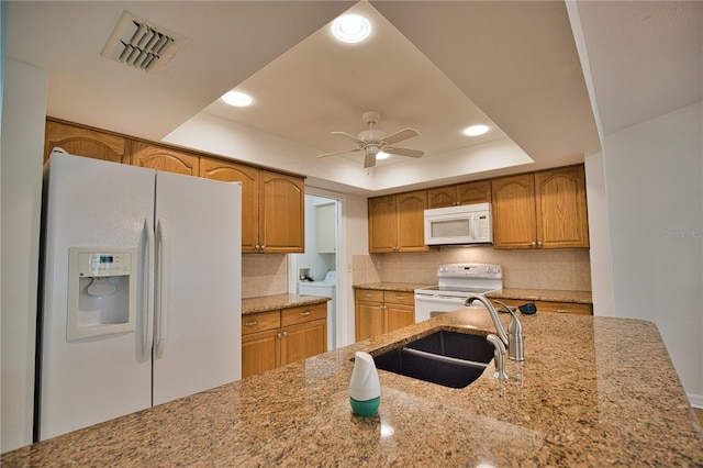 kitchen featuring light stone countertops, white appliances, sink, and a tray ceiling