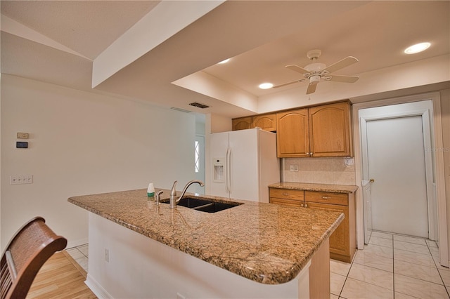 kitchen with a center island with sink, sink, ceiling fan, white fridge with ice dispenser, and light stone counters