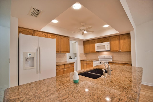 kitchen with light stone countertops, a raised ceiling, backsplash, white appliances, and light wood-type flooring