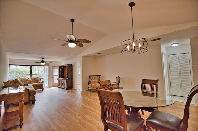 dining room with ceiling fan with notable chandelier, lofted ceiling, and light wood-type flooring