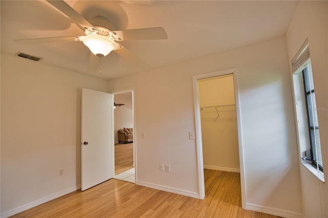 unfurnished bedroom with a closet, a spacious closet, light hardwood / wood-style flooring, and ceiling fan