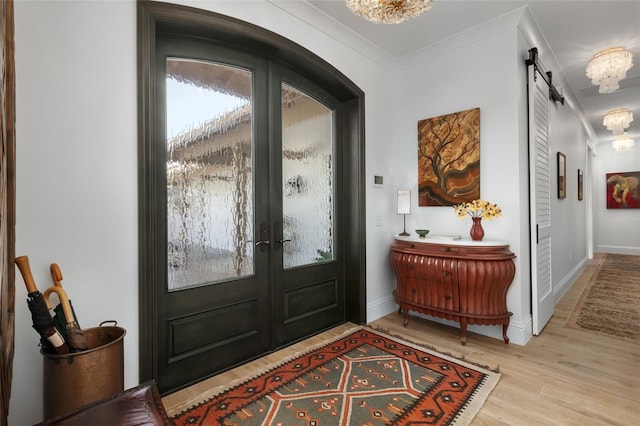 foyer entrance featuring a barn door, french doors, light hardwood / wood-style floors, and ornamental molding