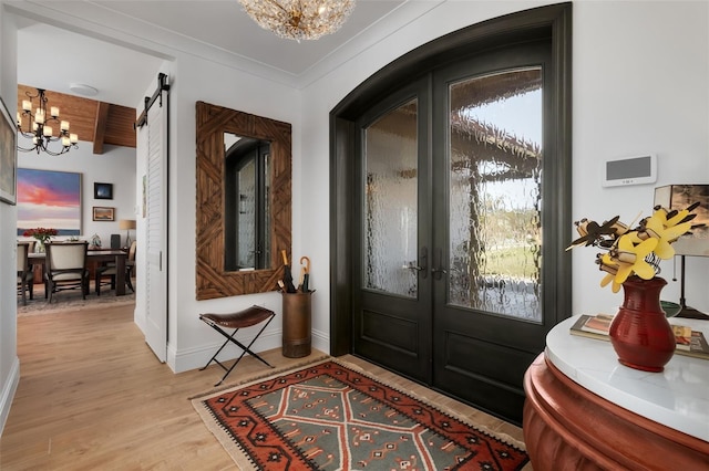 entryway featuring french doors, light wood-type flooring, ornamental molding, a barn door, and a notable chandelier