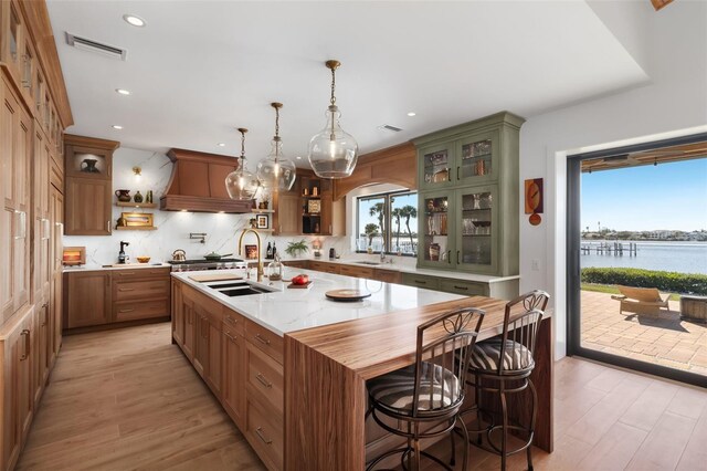 kitchen with premium range hood, a wealth of natural light, a kitchen island with sink, sink, and a water view