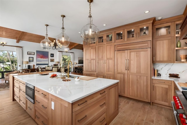 kitchen featuring beamed ceiling, plenty of natural light, light hardwood / wood-style floors, and an island with sink