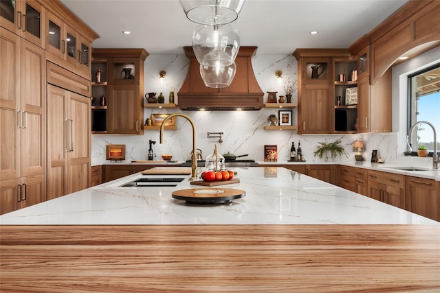 kitchen featuring light stone countertops, sink, tasteful backsplash, premium range hood, and pendant lighting