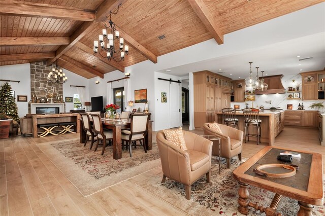 dining room with light wood-type flooring, wood ceiling, beam ceiling, a barn door, and a stone fireplace