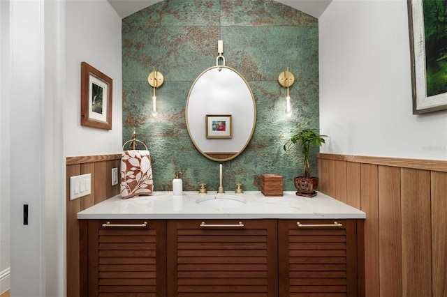 bathroom with vanity, wood walls, and lofted ceiling