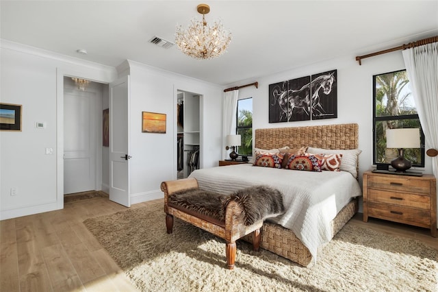 bedroom featuring a walk in closet, crown molding, light hardwood / wood-style floors, and an inviting chandelier