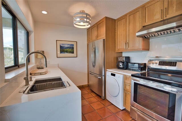 kitchen featuring sink, a textured ceiling, washer / dryer, light tile patterned floors, and appliances with stainless steel finishes