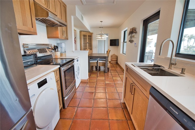 kitchen featuring appliances with stainless steel finishes, exhaust hood, sink, pendant lighting, and washer / dryer