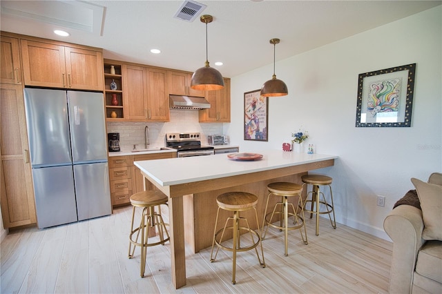 kitchen featuring backsplash, range hood, appliances with stainless steel finishes, decorative light fixtures, and a breakfast bar area