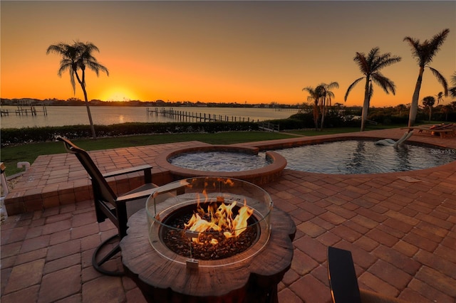 pool at dusk featuring a patio area, a water view, and an outdoor fire pit