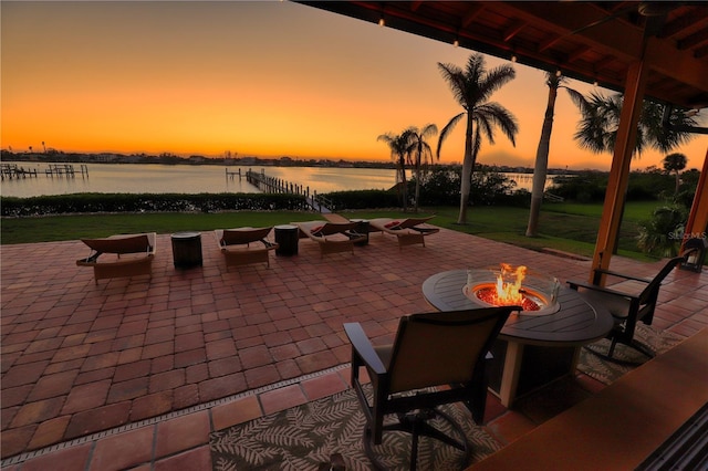 patio terrace at dusk with a fire pit, a water view, and a lawn