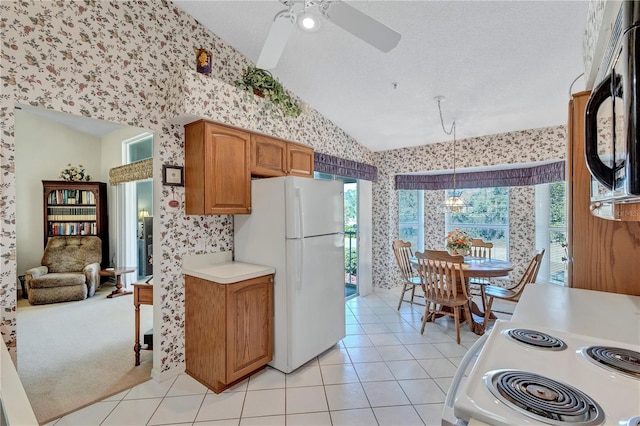 kitchen with stove, white refrigerator, hanging light fixtures, vaulted ceiling, and light tile patterned floors