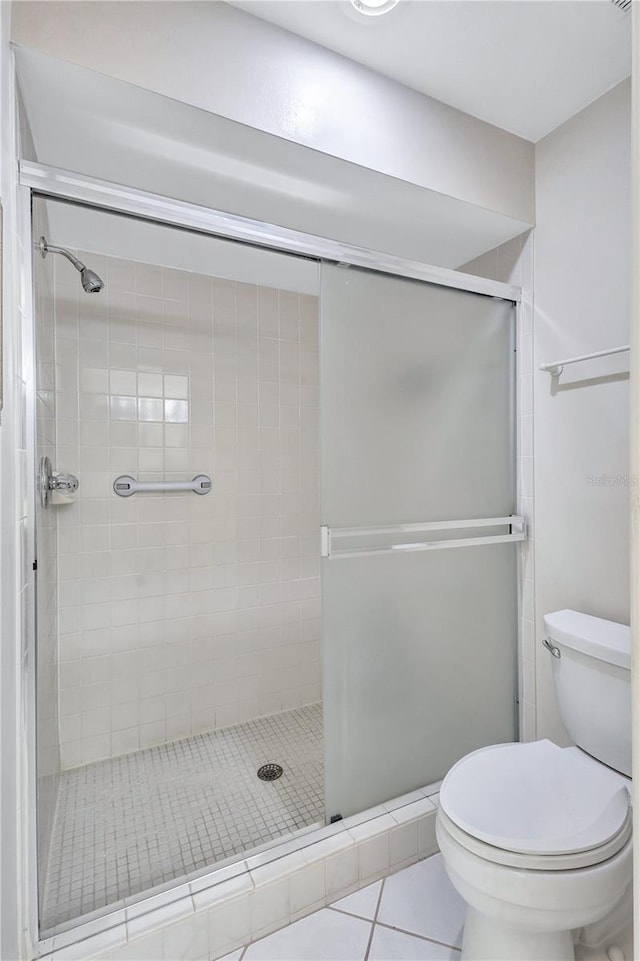 bathroom with tile patterned flooring, toilet, and a shower with shower door