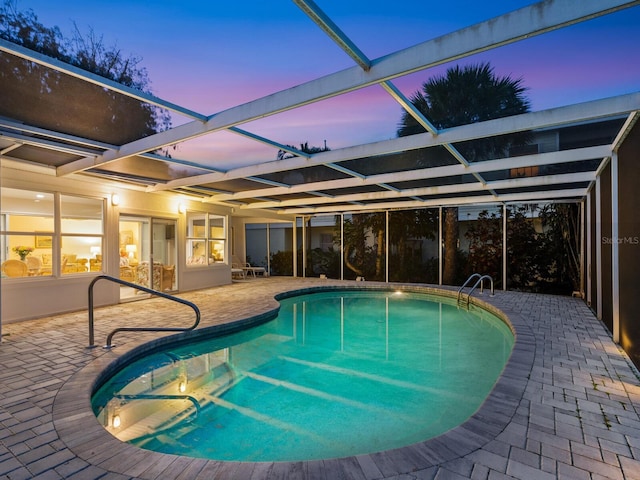 pool at dusk featuring a lanai and a patio