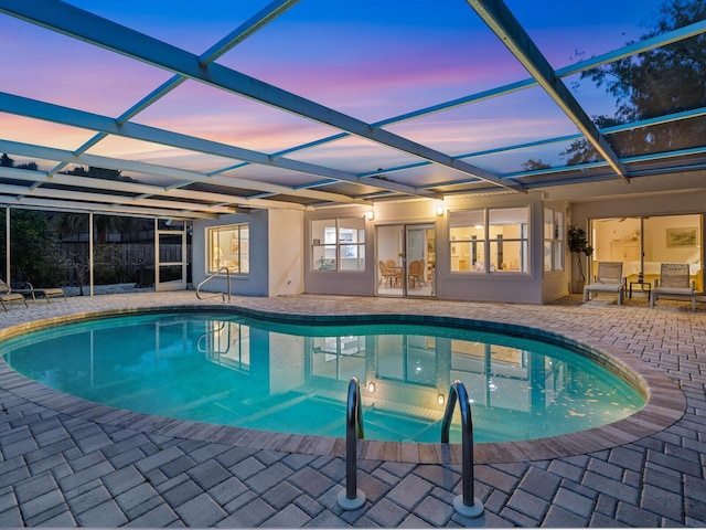 pool at dusk with a patio area and a lanai