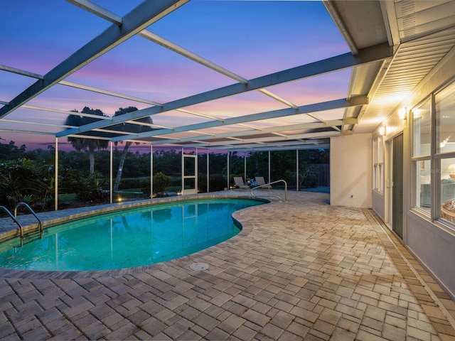 pool at dusk featuring a lanai and a patio area