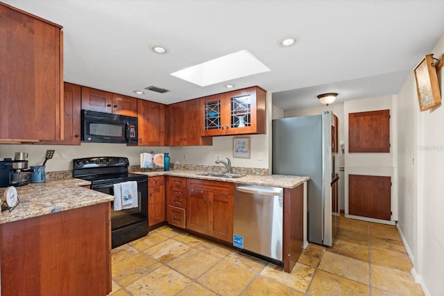 kitchen with a skylight, light stone counters, sink, and black appliances