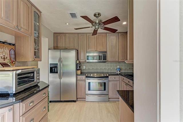 kitchen featuring ceiling fan, stainless steel appliances, light hardwood / wood-style flooring, dark stone counters, and decorative backsplash