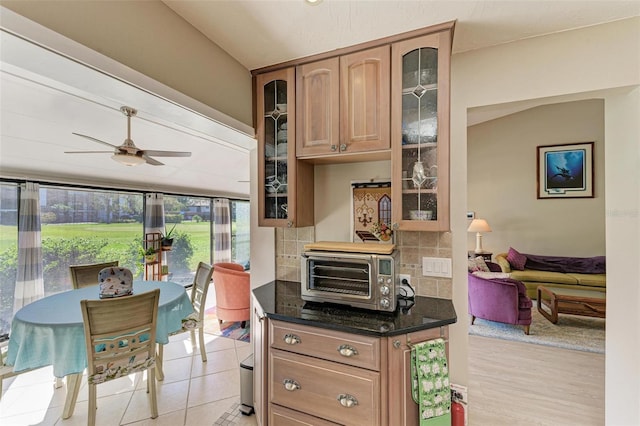 kitchen with ceiling fan, light hardwood / wood-style floors, dark stone counters, and tasteful backsplash