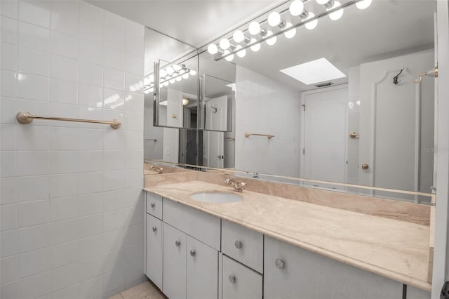 bathroom featuring tile patterned flooring, vanity, tile walls, and a skylight