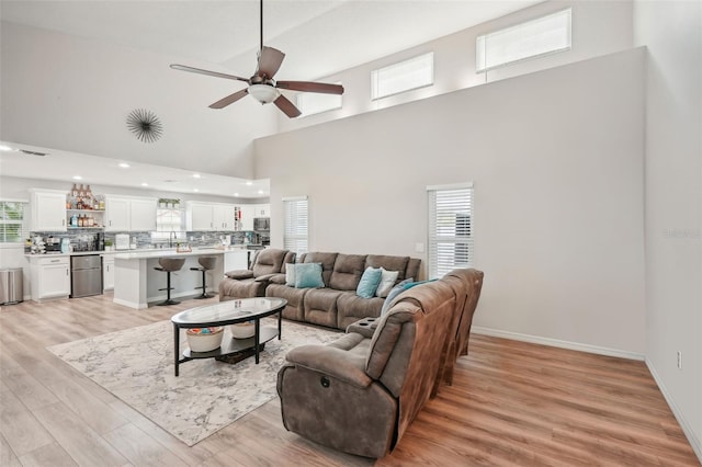 living room with a towering ceiling, light hardwood / wood-style flooring, ceiling fan, and sink