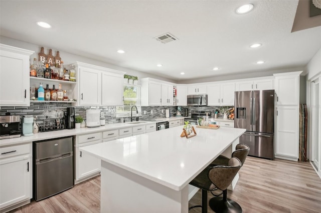 kitchen with sink, white cabinets, light hardwood / wood-style floors, a kitchen island, and appliances with stainless steel finishes