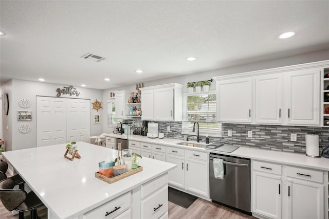 kitchen featuring dishwasher, sink, light wood-type flooring, a kitchen island, and white cabinetry