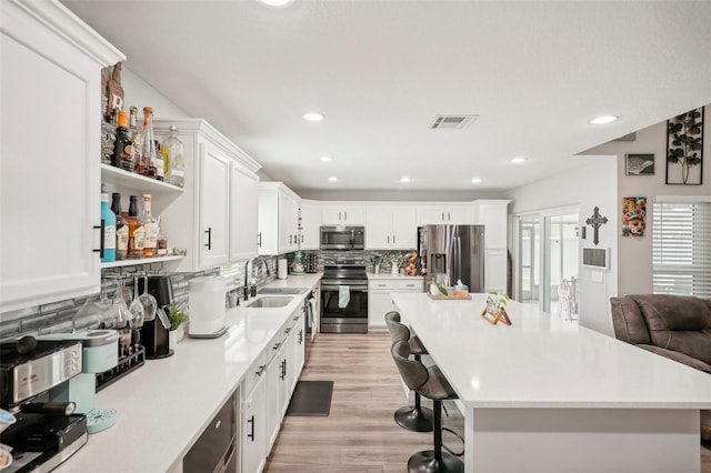 kitchen with backsplash, a kitchen breakfast bar, sink, appliances with stainless steel finishes, and light hardwood / wood-style floors