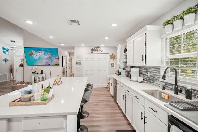 kitchen featuring light wood-type flooring, sink, white cabinets, black dishwasher, and a breakfast bar area