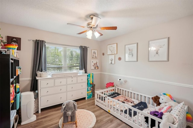 bedroom featuring a textured ceiling, ceiling fan, light hardwood / wood-style floors, and a crib