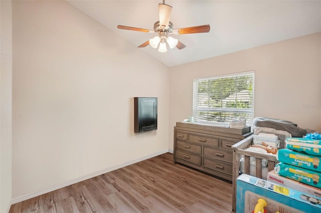 bedroom with a crib, ceiling fan, light hardwood / wood-style floors, and vaulted ceiling