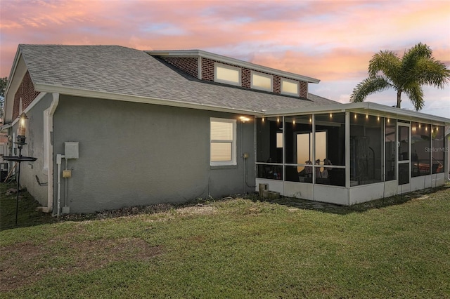 back house at dusk with a sunroom and a yard