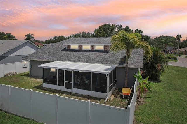 back house at dusk with a lawn and a sunroom