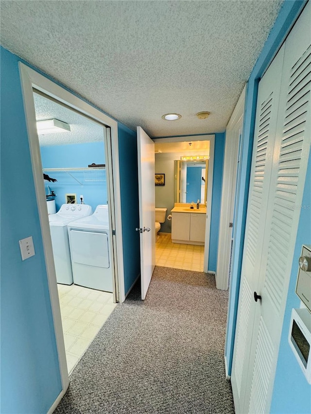 hall featuring washer and clothes dryer, light colored carpet, and a textured ceiling