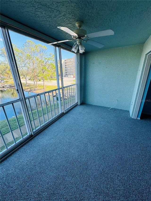 unfurnished sunroom with ceiling fan, a water view, and a wealth of natural light