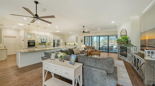 living room with a fireplace, sink, ceiling fan, crown molding, and dark wood-type flooring