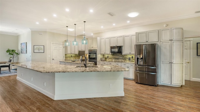 kitchen with light stone counters, decorative light fixtures, a large island with sink, and black appliances