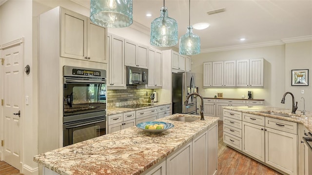 kitchen featuring a kitchen island with sink, sink, light stone counters, and black appliances