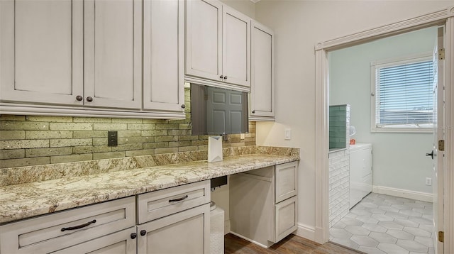 kitchen with light tile patterned floors, tasteful backsplash, light stone countertops, white cabinets, and washing machine and clothes dryer