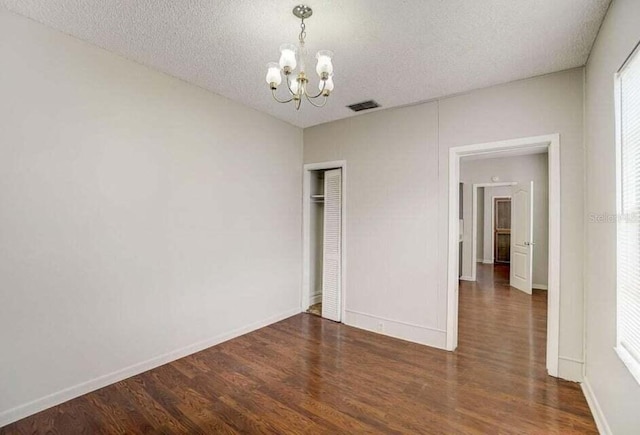 unfurnished bedroom with a textured ceiling, a notable chandelier, dark wood-type flooring, and a closet